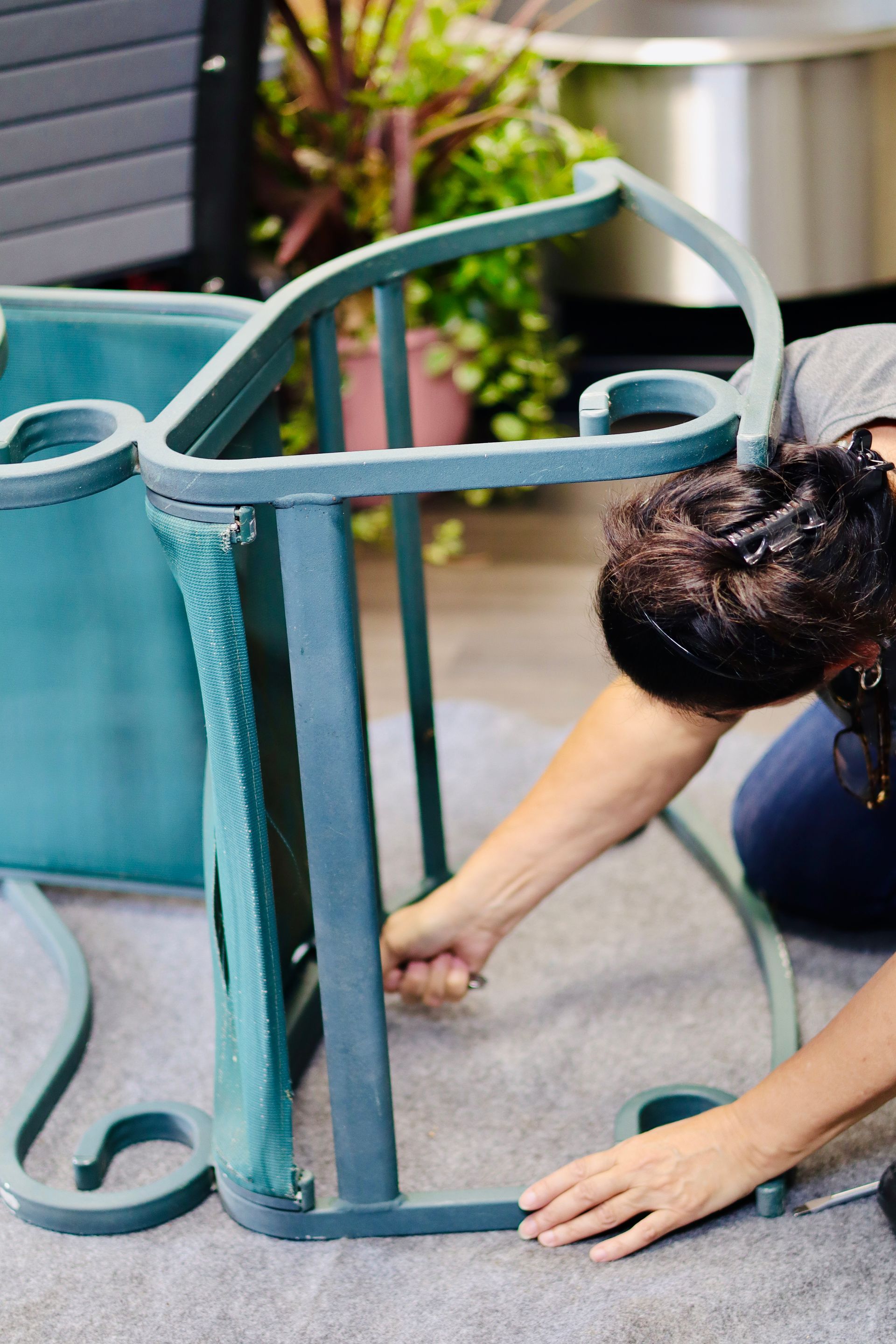 Person assembling a green metal patio chair on a deck