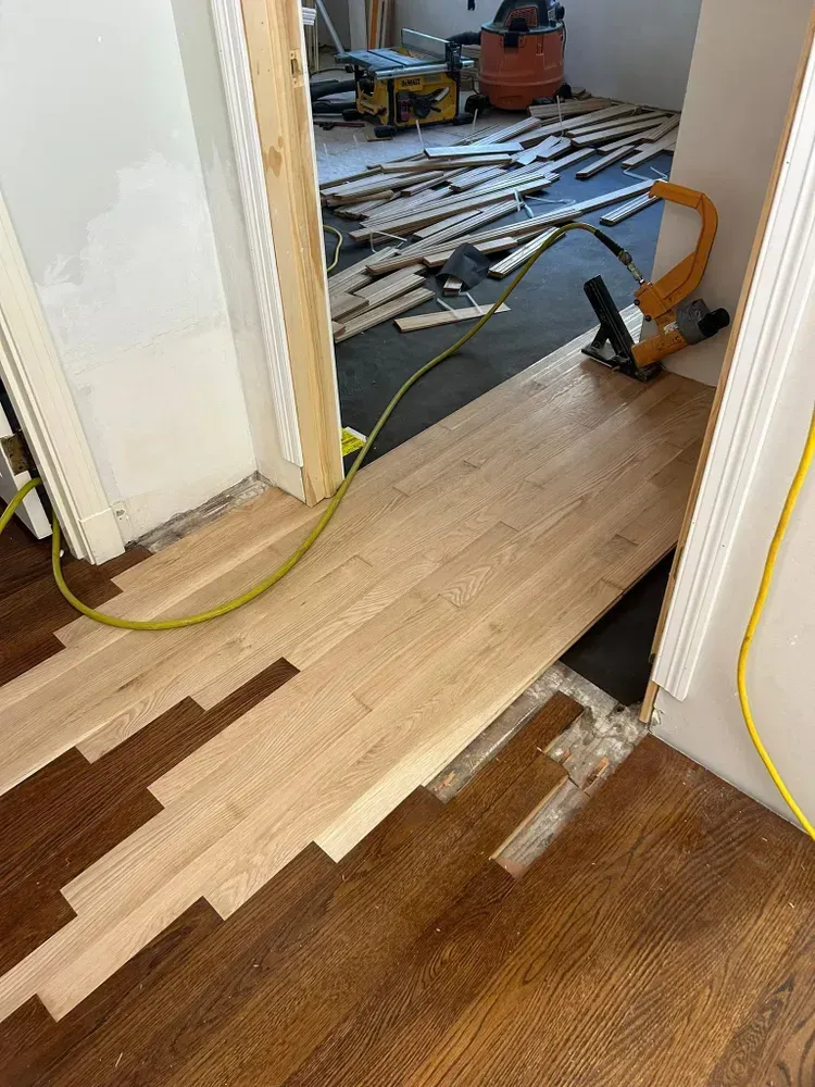 A view of a doorway transition where light unfinished wood flooring is being installed to meet existing dark wood floors.