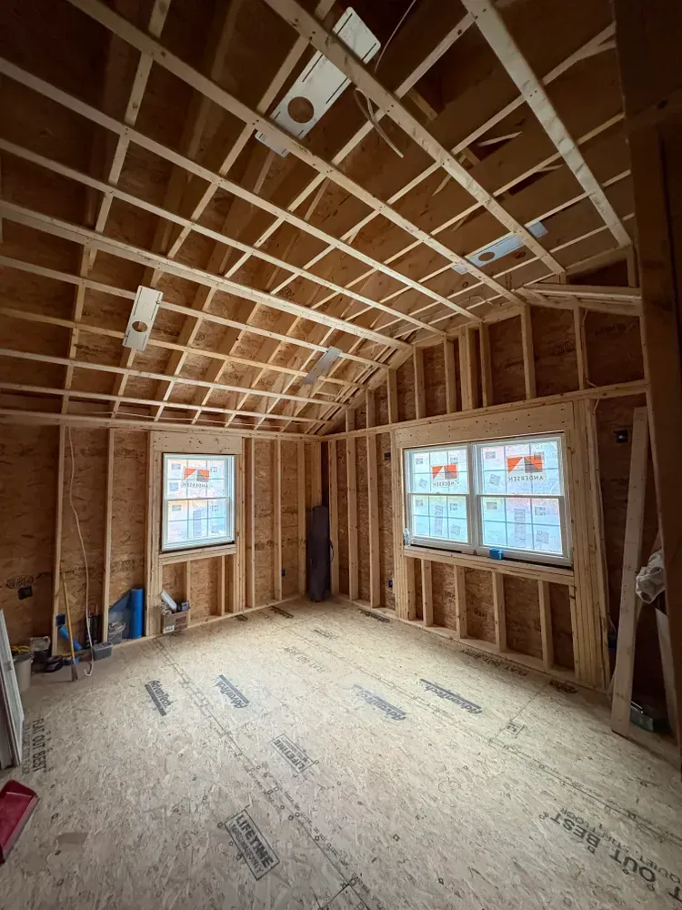 Unfinished room interior featuring wood-framed walls and vaulted ceilings with two installed windows and plywood flooring.