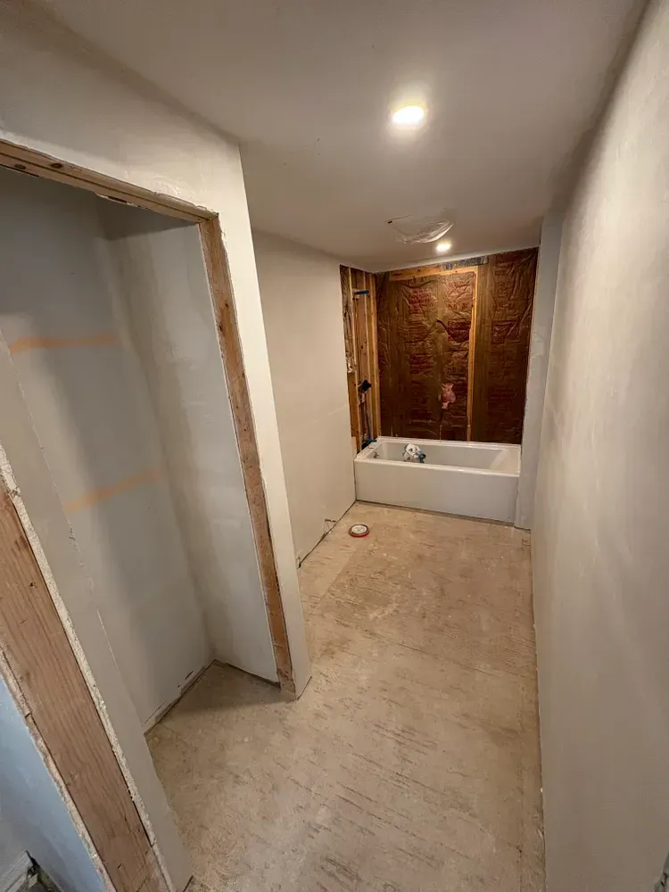 An interior view of a room under construction, featuring white walls, an unfinished doorway, and a white bathtub.