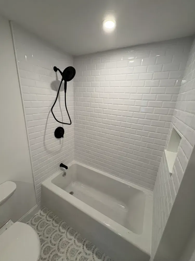 A modern bathroom featuring a white subway-tile bathtub enclosure, black fixtures, and a decorative patterned floor.
