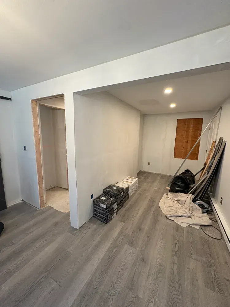 Renovated room with grey wood-look flooring, freshly painted white walls, an open doorway, and construction supplies.