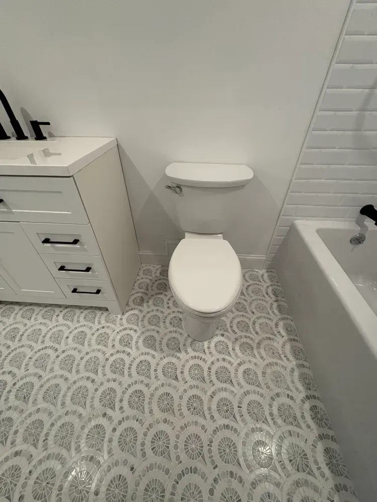 A bathroom featuring a white vanity, toilet, and bathtub with decorative, patterned floor tiles.