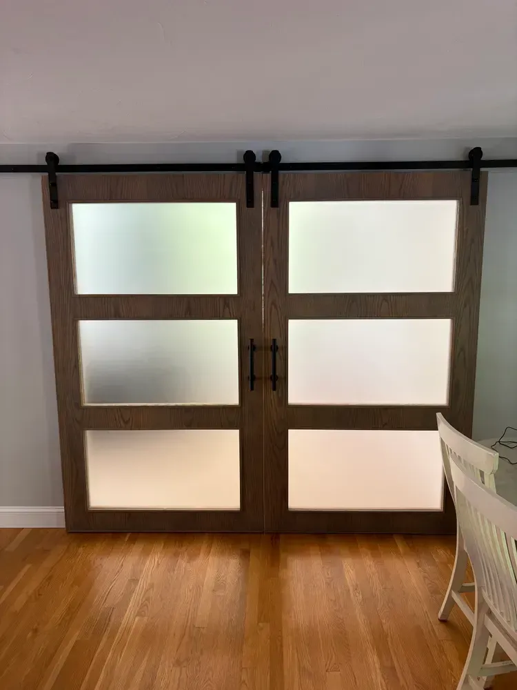 Two brown, three-paneled frosted glass sliding barn doors mounted on a black rail, positioned against a gray wall.