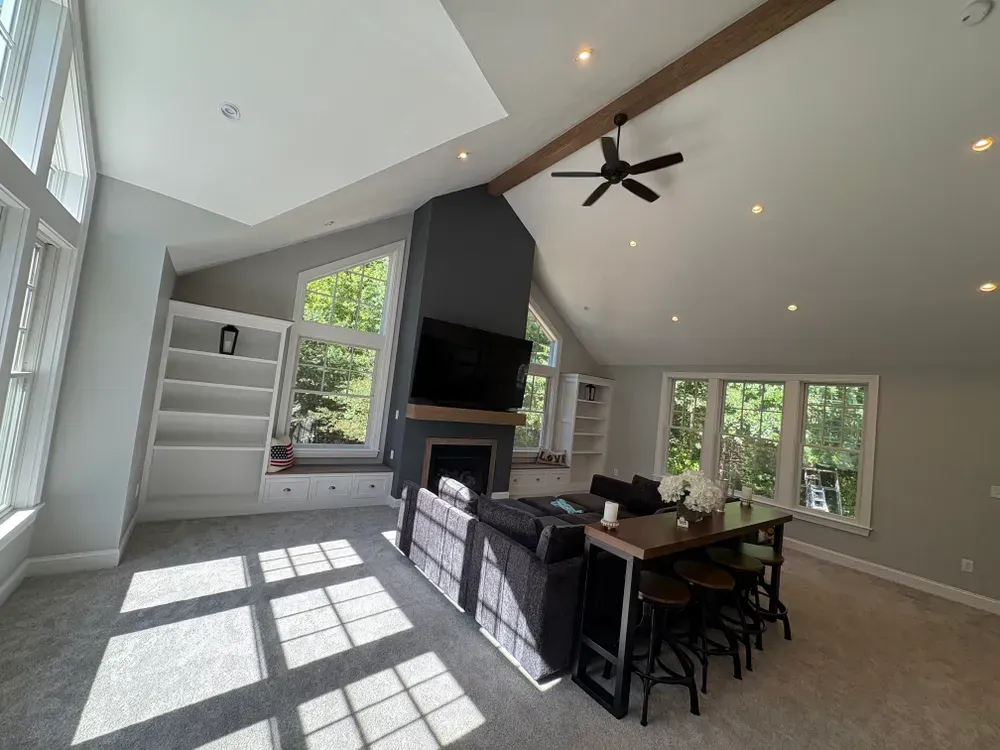 A modern, bright living room features a vaulted ceiling, gray accent wall with a fireplace, large windows, and a sofa.