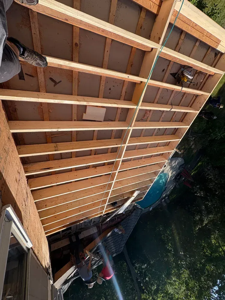 A high-angle view of a wooden deck frame being constructed next to a brick house and an outdoor swimming pool.