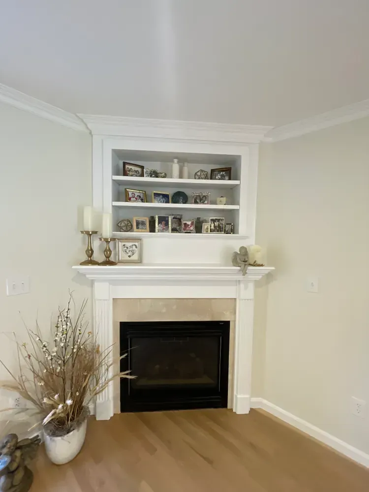 A fireplace with a white mantel and built-in shelving filled with small framed photos, located in a corner of a room.