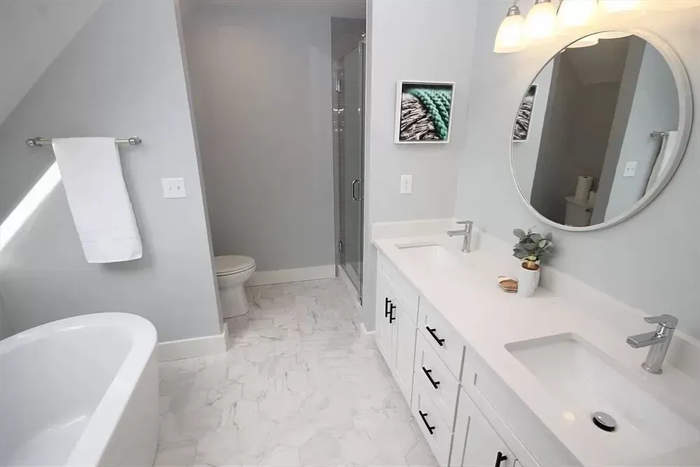 A modern bathroom featuring a white vanity with a round mirror, a freestanding tub, and a separate shower area.