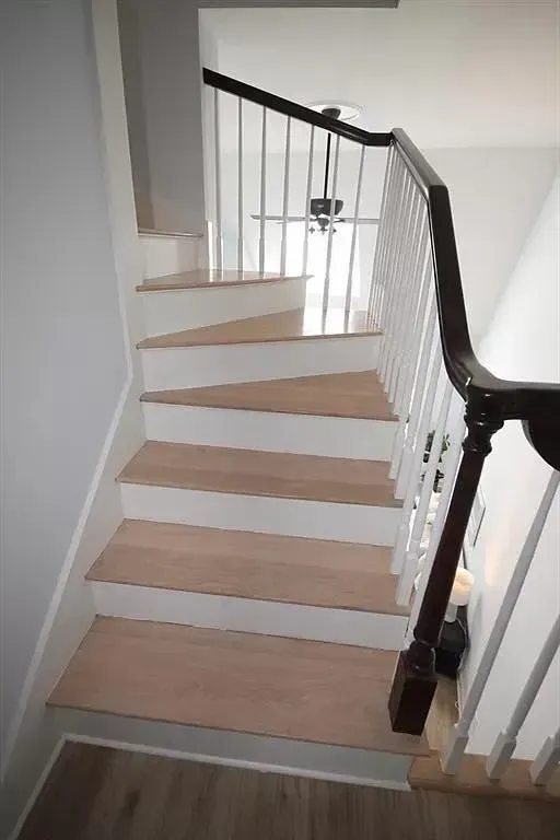 A wooden staircase with white risers and a dark handrail, viewed from the bottom looking up toward a landing.