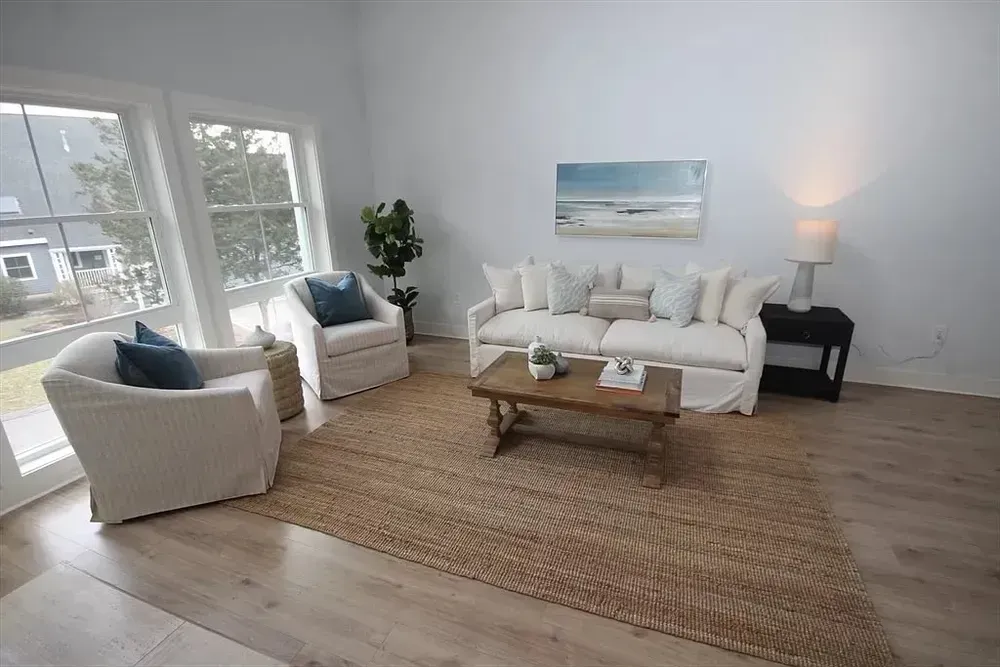 A bright, airy living room with a beige sofa, two matching armchairs, a wooden coffee table, and a large jute rug.