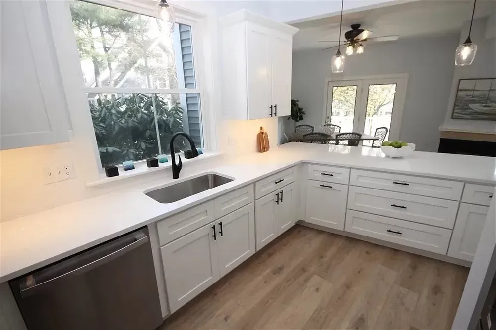 A bright, modern kitchen featuring white shaker cabinets, white countertops, stainless appliances, and wood-look flooring.
