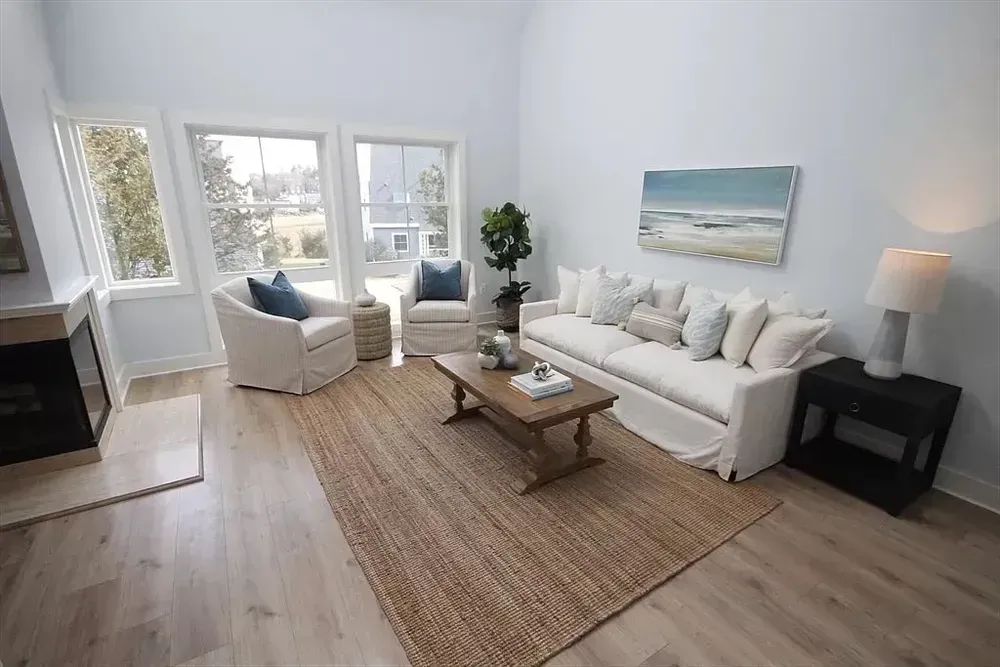 A bright living room features a white sofa, two armchairs, a wooden coffee table, and a rug on light wood floors.