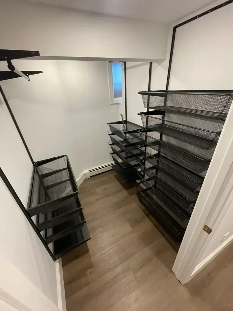A walk-in closet featuring black metal shelving units and hanging rods against white walls and light wood flooring.