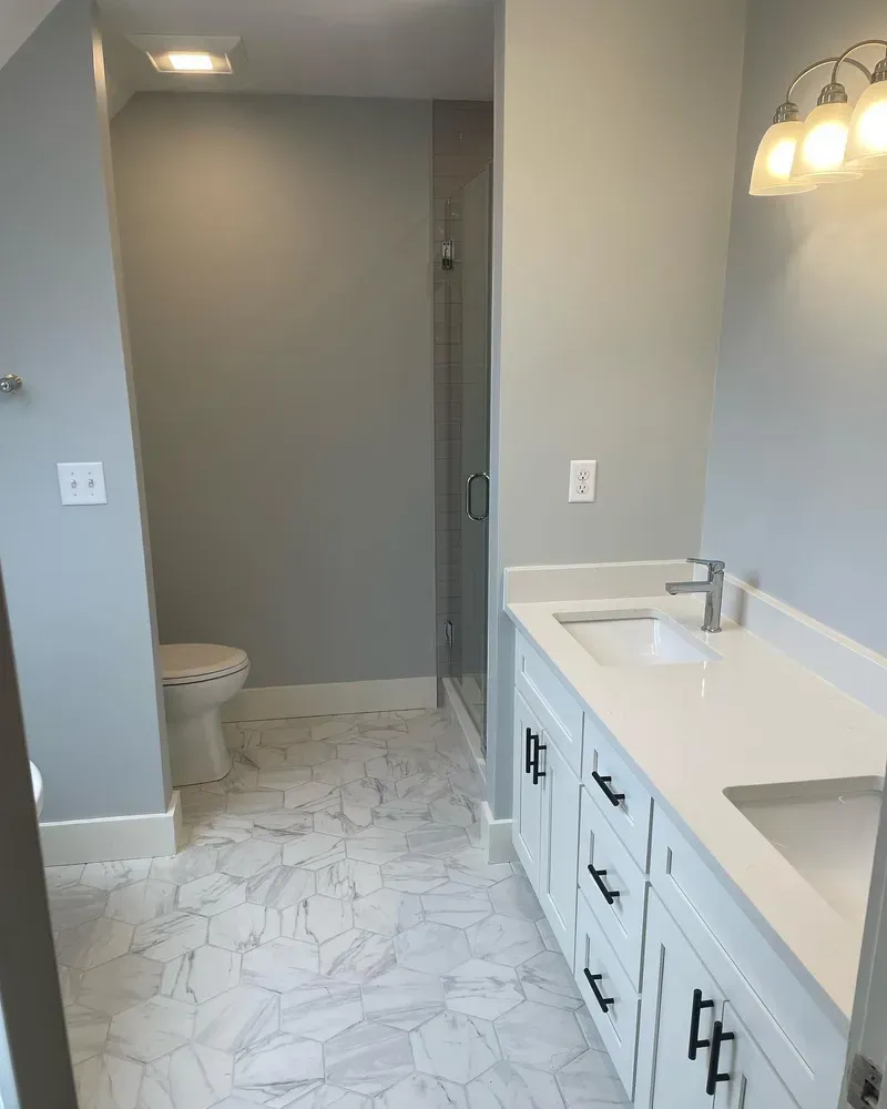 A modern bathroom featuring white marble hexagon floors, a white vanity with black hardware, and a separate shower area.