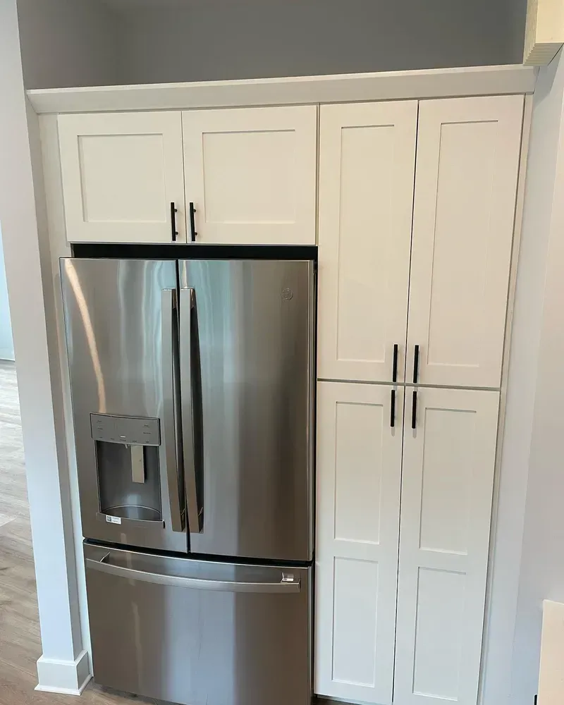 A stainless steel French-door refrigerator built into white cabinetry in a modern kitchen.