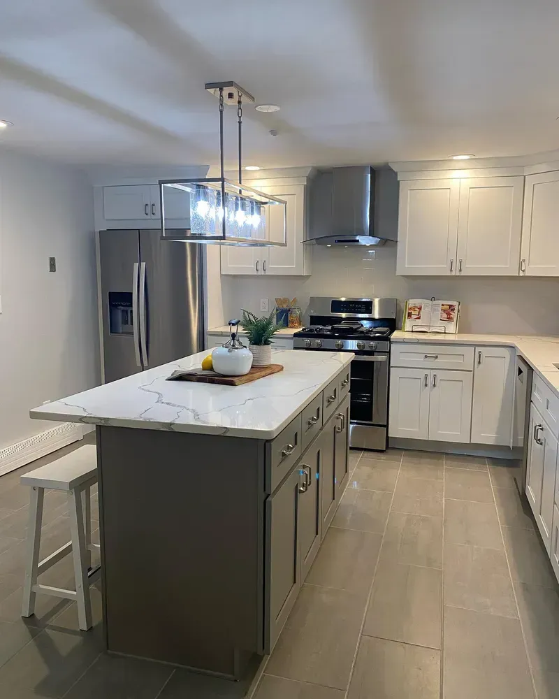 A modern kitchen features a central white marble-topped island, white cabinetry, stainless appliances, and tile flooring.