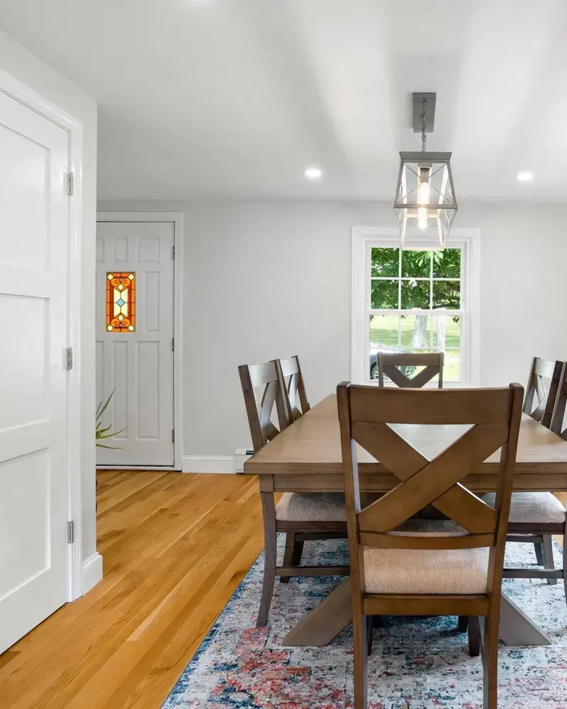 A dining room with a wooden table, chairs with cross-back details, and a patterned rug on a hardwood floor.