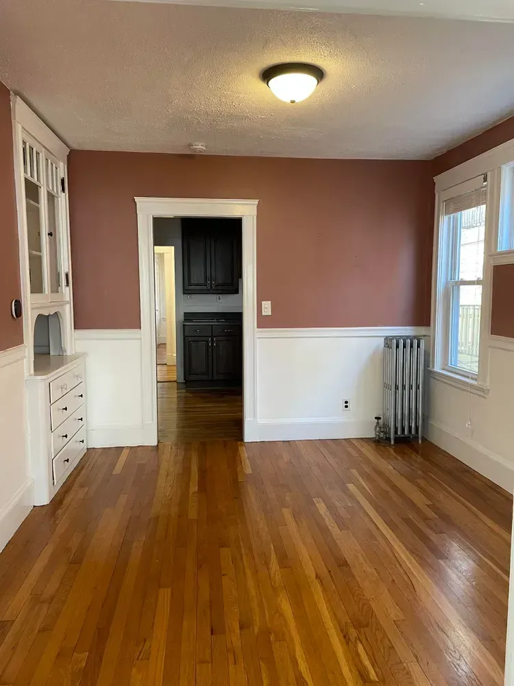 Dining room with wood floors, two-toned terracotta and white walls, built-in cabinetry, and a radiator by the window.