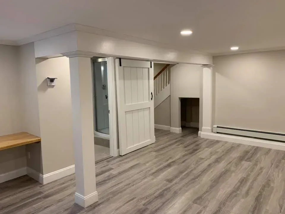 A basement interior with light wood-look flooring, beige walls, a white sliding barn door, and a built-in wooden desk.