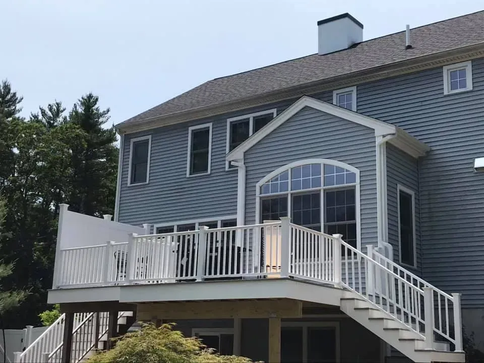Blue, two-story suburban house with a large white composite deck and staircase leading to the backyard.