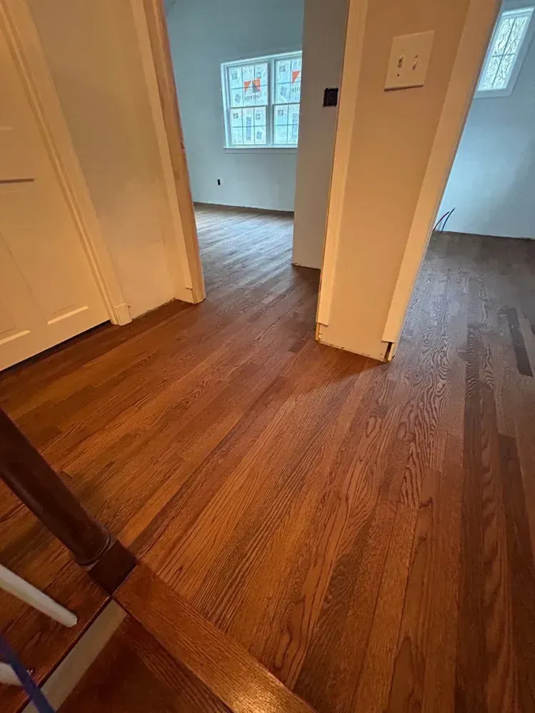 A hallway with polished hardwood floors leads through an open doorway into a room with a window.