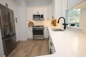 Modern kitchen with white cabinets, stainless steel appliances, white countertops, and a black faucet.