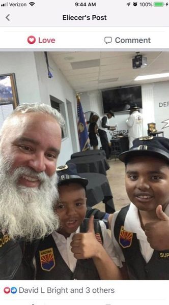 Man with beard and two children giving thumbs up, wearing uniforms, indoors.