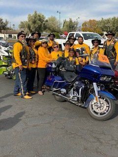 Group of people in yellow shirts pose with blue motorcycle outdoors.