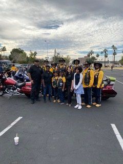 Group of people wearing yellow vests pose with motorcycles in a parking lot. Cloudy sky.