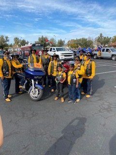 Group of motorcyclists in yellow vests pose with a blue motorcycle, outdoors in a parking lot.