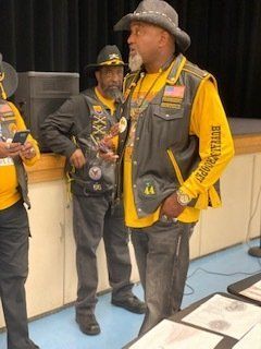 Men in vests and hats, possibly at an event. One man has a yellow shirt that reads 