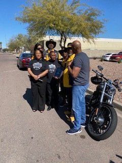 Group of people near a motorcycle; some wearing yellow; outdoors, sunny day.