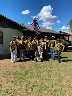 Group of people in yellow vests pose in front of a house with an American flag.