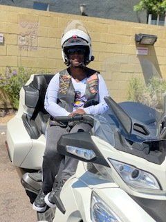 Person wearing a helmet sits on a white motorcycle, a building in the background.