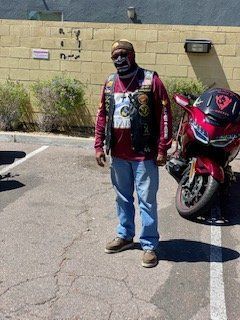 Man in biker vest standing next to a red motorcycle in a parking lot.