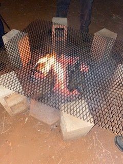Fire burning under a metal grill, supported by cinder blocks.