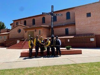 Group of people in yellow vests stand in front of a brick church with a cross.