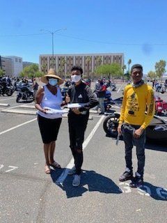Woman with two young men in a parking lot holding papers, possibly an event or check presentation.