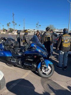 Group of people gathered around blue motorcycle; sunny outdoor setting.