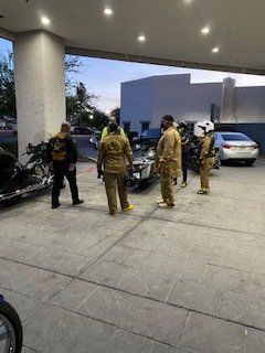 Group of people near a damaged car under a building overhang; two motorcycles visible.