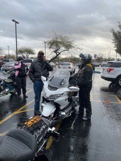 People near motorcycles in a wet parking lot, cloudy skies. One person is on the phone.