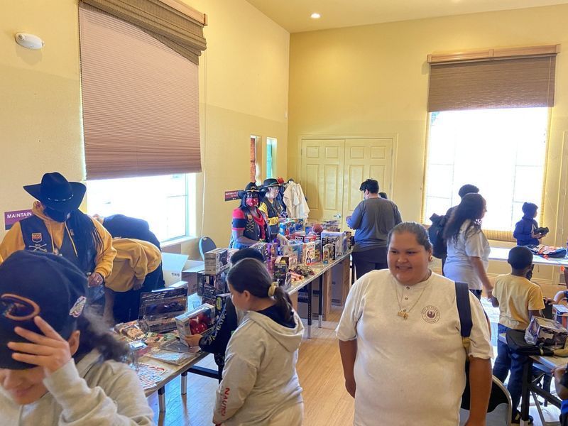 People browsing tables of items at an indoor sale, in a room with windows and light walls.