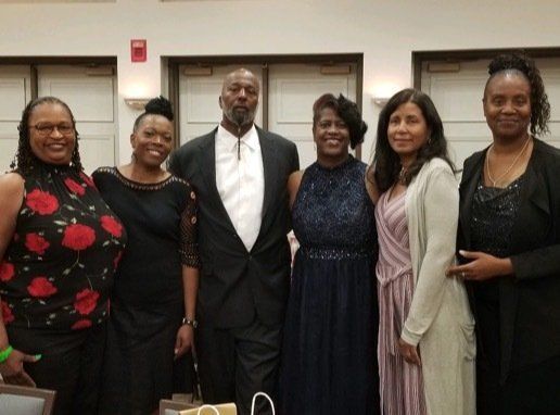 Group of six people posing for a photo indoors; dressed in formal attire.