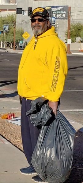 Person in yellow hoodie holding a large black trash bag on a sidewalk.