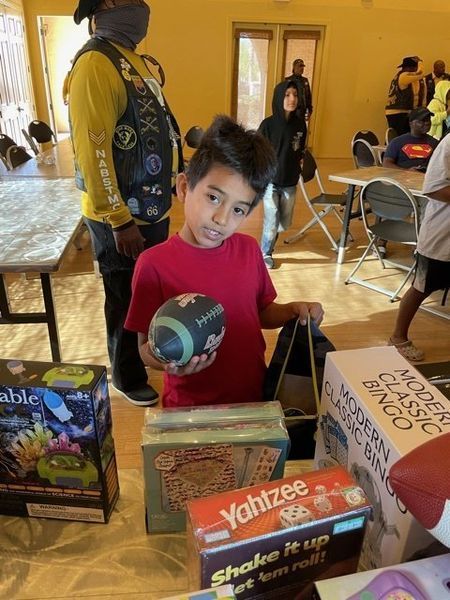 Boy holding a football, surrounded by board games. Interior, sunlight, and other people in the background.