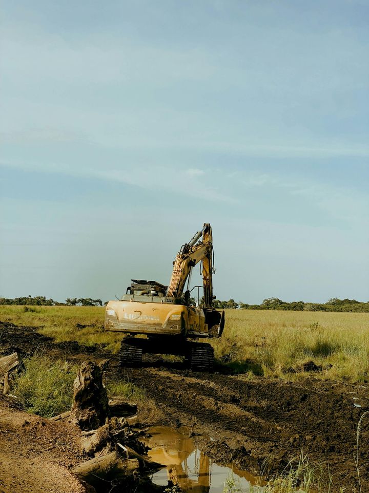 Excavator working in a muddy field under a clear blue sky