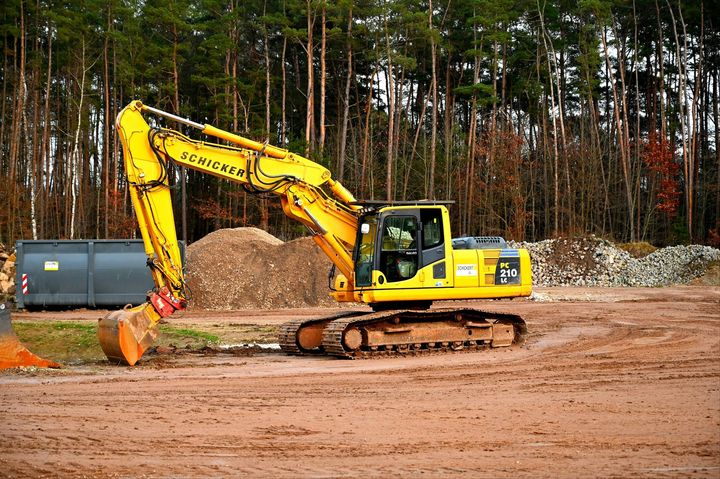 Yellow excavator digging dirt at a construction site with trees in the background