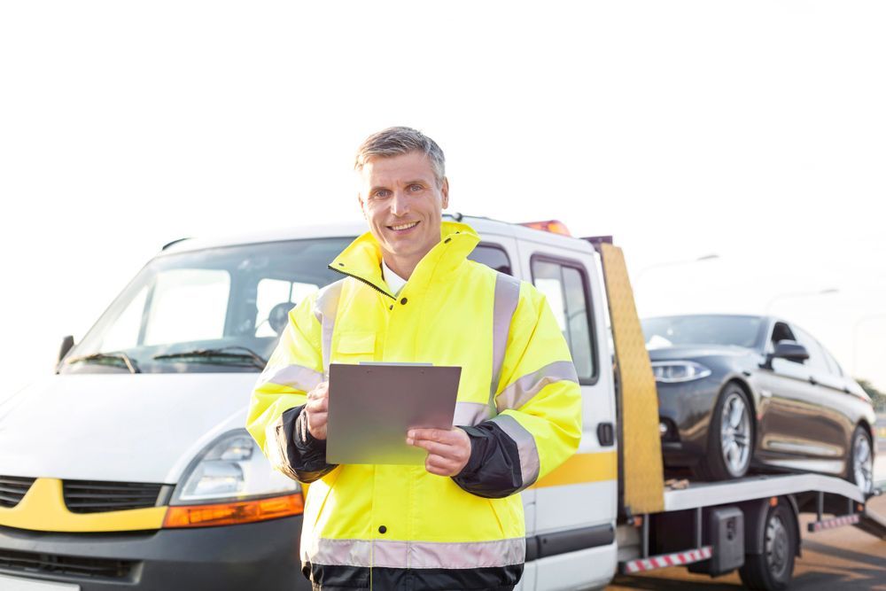 A Man Is Standing In Front Of A Tow Truck Holding A Tablet — Gympie/Childers Towing Pty Ltd in Gympie, QLD