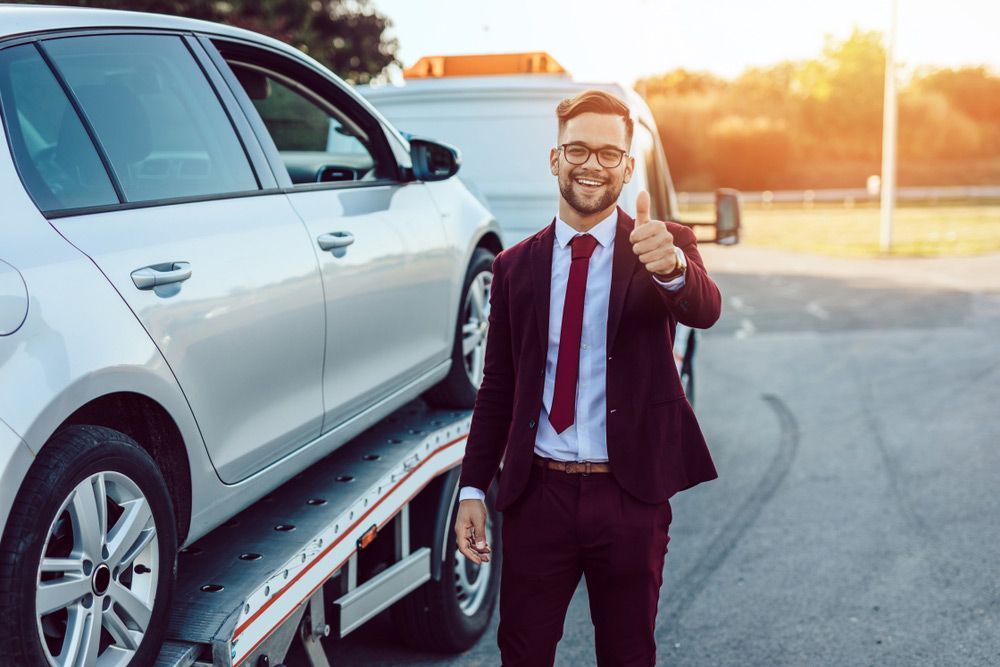 A Man In A Suit And Tie Is Giving A Thumbs Up Next To A Tow Truck — Gympie/Childers Towing Pty Ltd in Maryborough, QLD