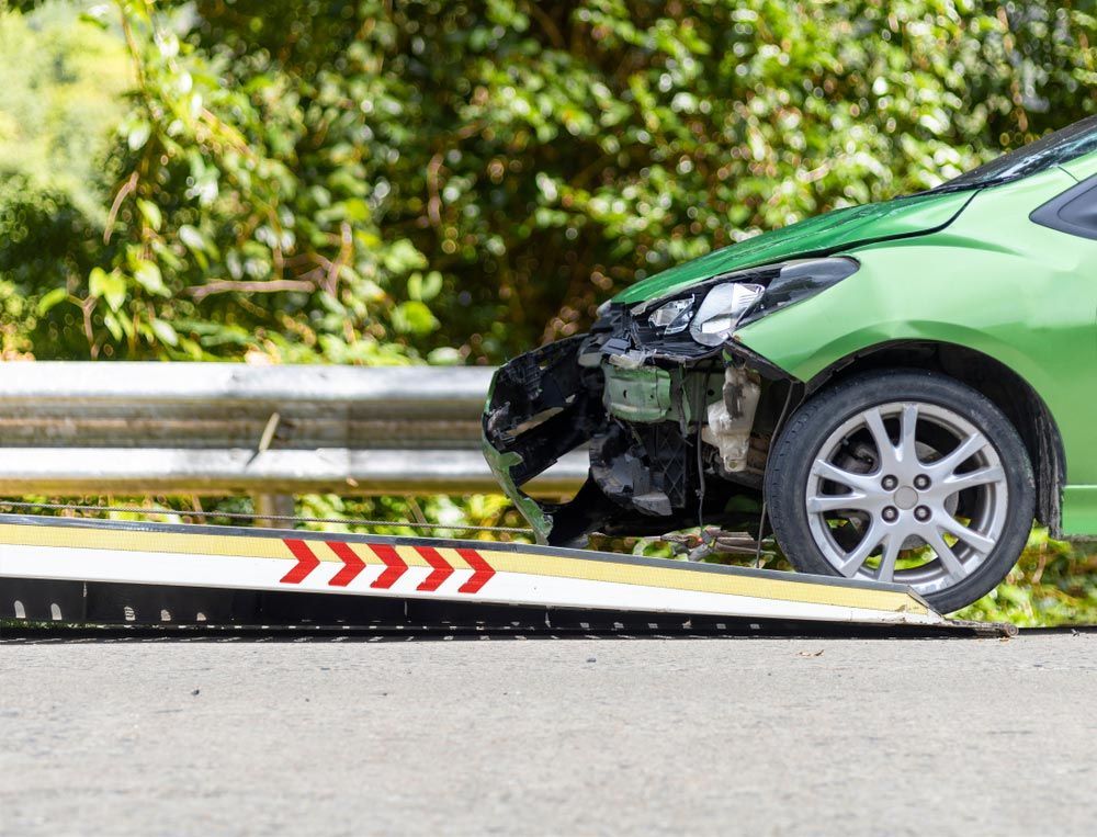 A Green Car Is Being Towed By A Tow Truck — Gympie/Childers Towing Pty Ltd in Kybong, QLD
